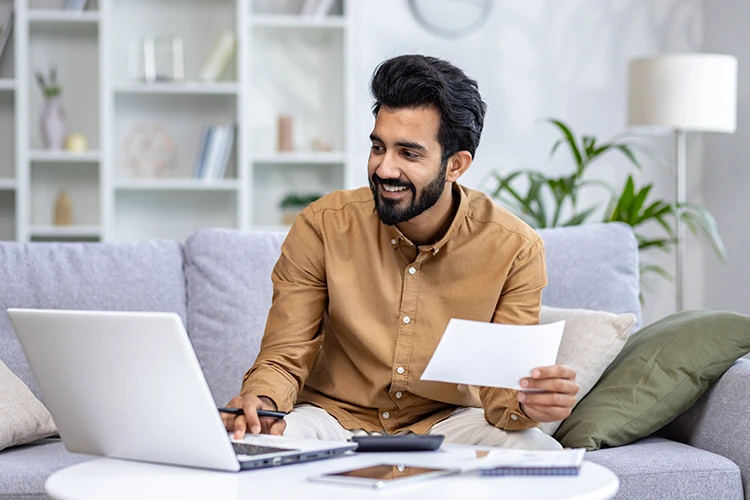 a man working on his laptop while holding a piece of paper