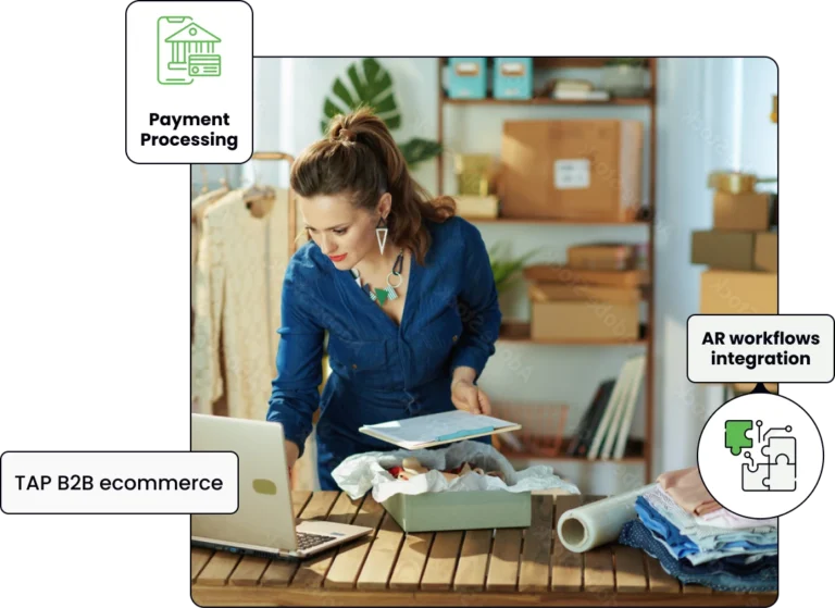 woman standing in a shop, working on her laptop while holding a clipboard with some to-be-delivered products lying nearby