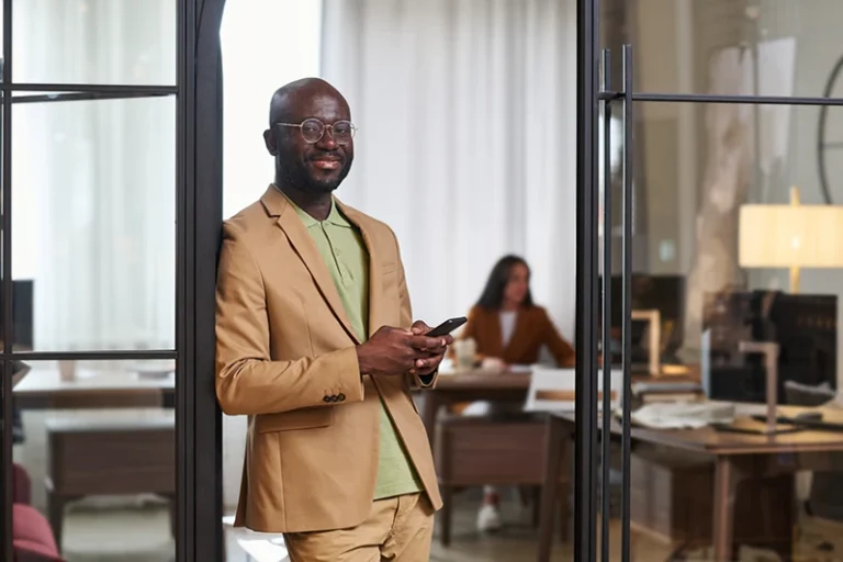 a smiling man standing and holding his phone in an office