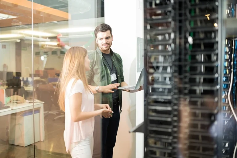 a man with a laptop talking to a woman while standing in a server room